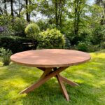 Ronde tuintafel gemaakt van teakhout. De tafel heeft een kruispoot