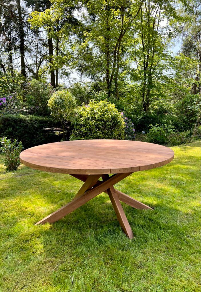 Ronde tuintafel gemaakt van teakhout. De tafel heeft een kruispoot